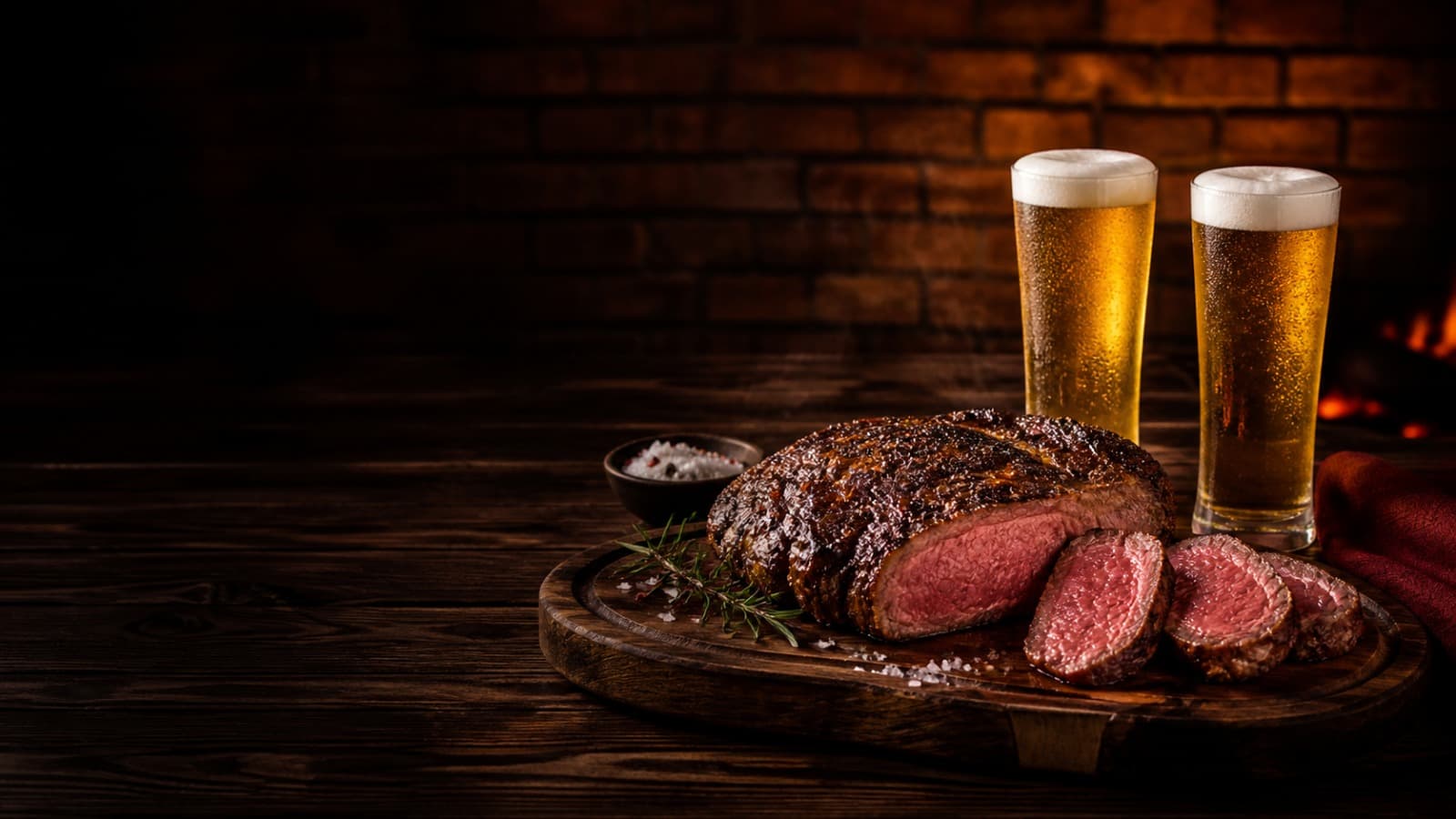 Corte de carne grelhado e fatiado ao lado de dois copos de chope gelados, sobre tábua de madeira